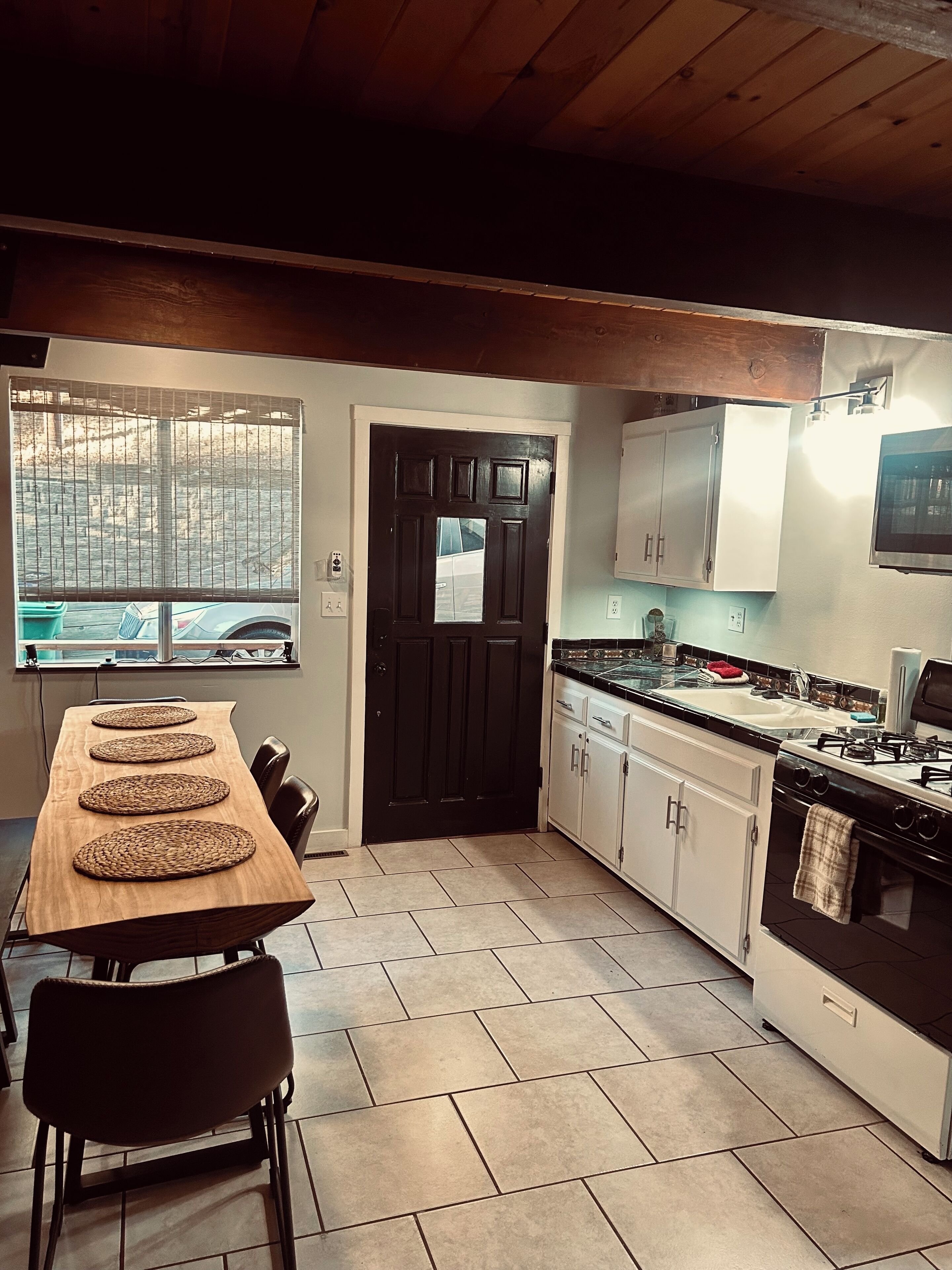 A kitchen with a wooden table, chairs, a stove, cabinets, and a window with blinds.