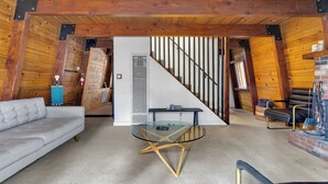 A cozy room with a wooden ceiling, a glass coffee table, a sofa, and a staircase leading to another level. - CRESCENT TREE CABIN CLOSE TO BEAR MOUNTAIN, GOLF COURSE  AND THE ZOO (Big Bear Lake)