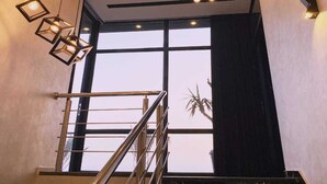 Eine Treppe mit Metallgeländern, Blick zum Himmel durch große Fenster und hängende geometrische Leuchten.