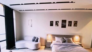 Ein modernes Schlafzimmer mit einer gebogenen Couch, einem Bett mit Holzkopfteil und einem Nachttisch.