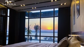 Ein Schlafzimmer mit großem Fenster mit Blick auf ein Gewässer und einen Sonnenuntergang.