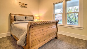 A bedroom with a wooden bed, a nightstand with a lamp, and a window with a view of trees. - Welcoming Helena Hideaway ~ 2 Mi to Downtown (Helena)