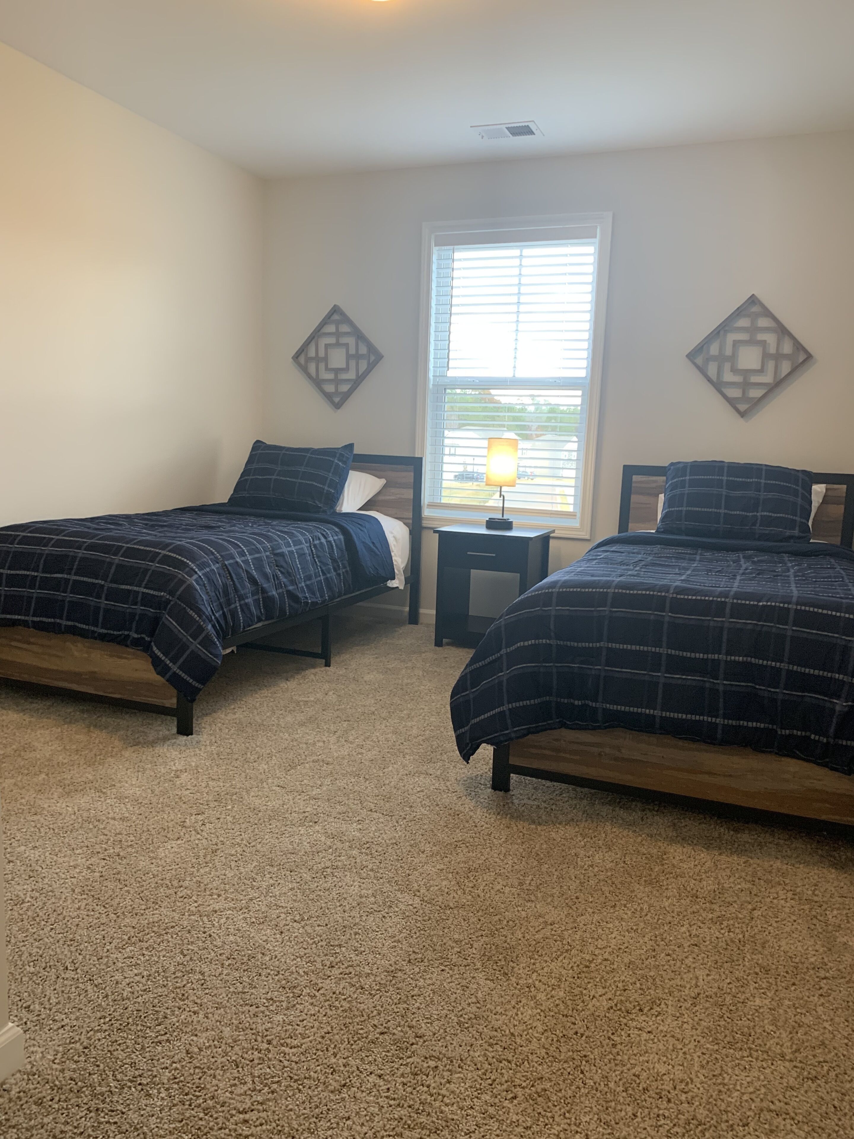 A bedroom with two beds, a window with blinds, and decorative wall art.