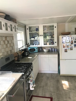 Una cocina con armarios blancos, un microondas azul, una estufa y un refrigerador.