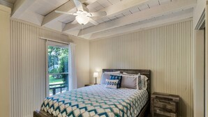 Een slaapkamer met een houten bed, een plafondventilator, een nachtkastje en uitzicht op de omgeving.