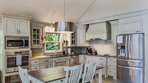 Een moderne keuken met witte kastjes, roestvrijstalen apparatuur en een houten eettafel.
