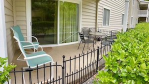 Un patio cubierto con puerta corrediza de vidrio, mobiliario exterior y valla de metal.