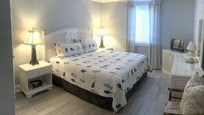 Un dormitorio con una cama, dos mesitas de noche con lámparas, un televisor, un escritorio con lámpara y una silla.