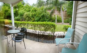 Une terrasse couverte, dotée d’une table et de chaises, entourée d’une clôture en métal et d’une végétation luxuriante.
