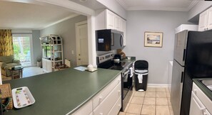 A compact kitchen with a green countertop, white cabinets, a microwave, a black trash bin, and a refrigerator. - E11 Peaceful 2/2 Ground Level, New Shower & Floors (St. Simons Island)