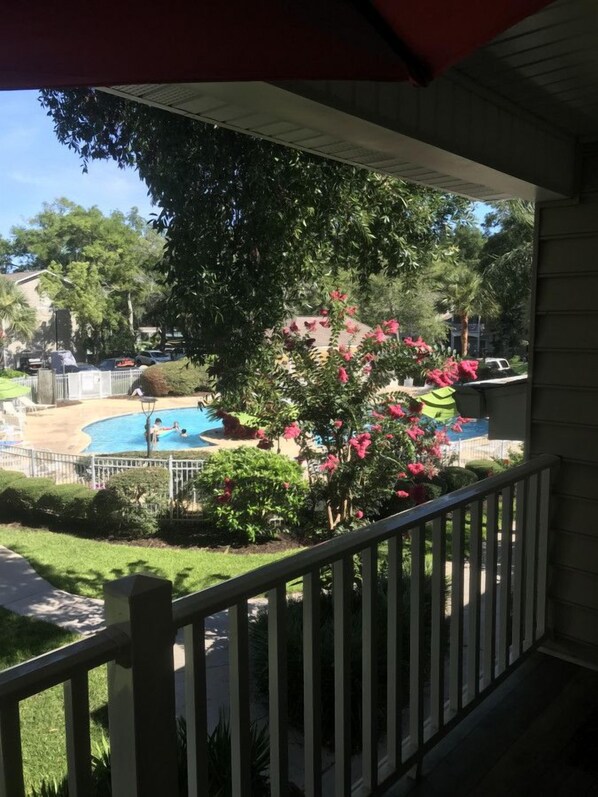 A covered outdoor area with a swimming pool, surrounded by lush greenery and flowering plants. - E11 Peaceful 2/2 Ground Level, New Shower & Floors (St. Simons Island)