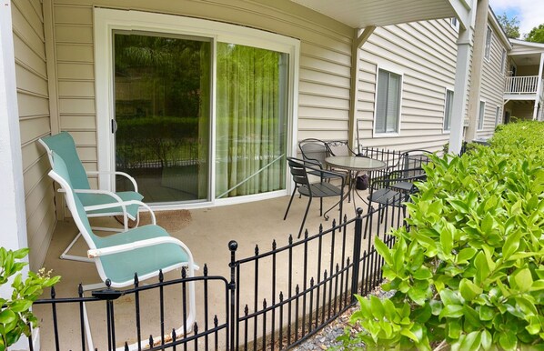 A covered patio with a sliding glass door, outdoor furniture, and a metal fence.
