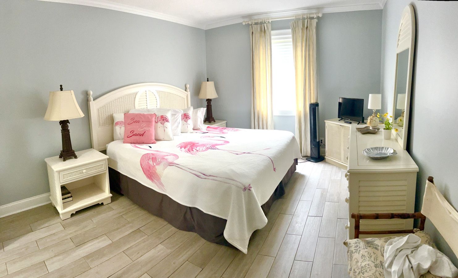 Un dormitorio con cama, mesitas de noche, cómoda, espejo y ventana con cortinas.
