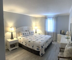 Une chambre à coucher comprenant un lit, deux tables de chevet avec des lampes, une télévision, un bureau avec une lampe et une chaise.