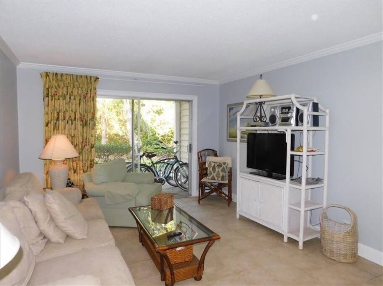 A living room with a sofa, a glass coffee table, a TV stand, and a bicycle outside the window.