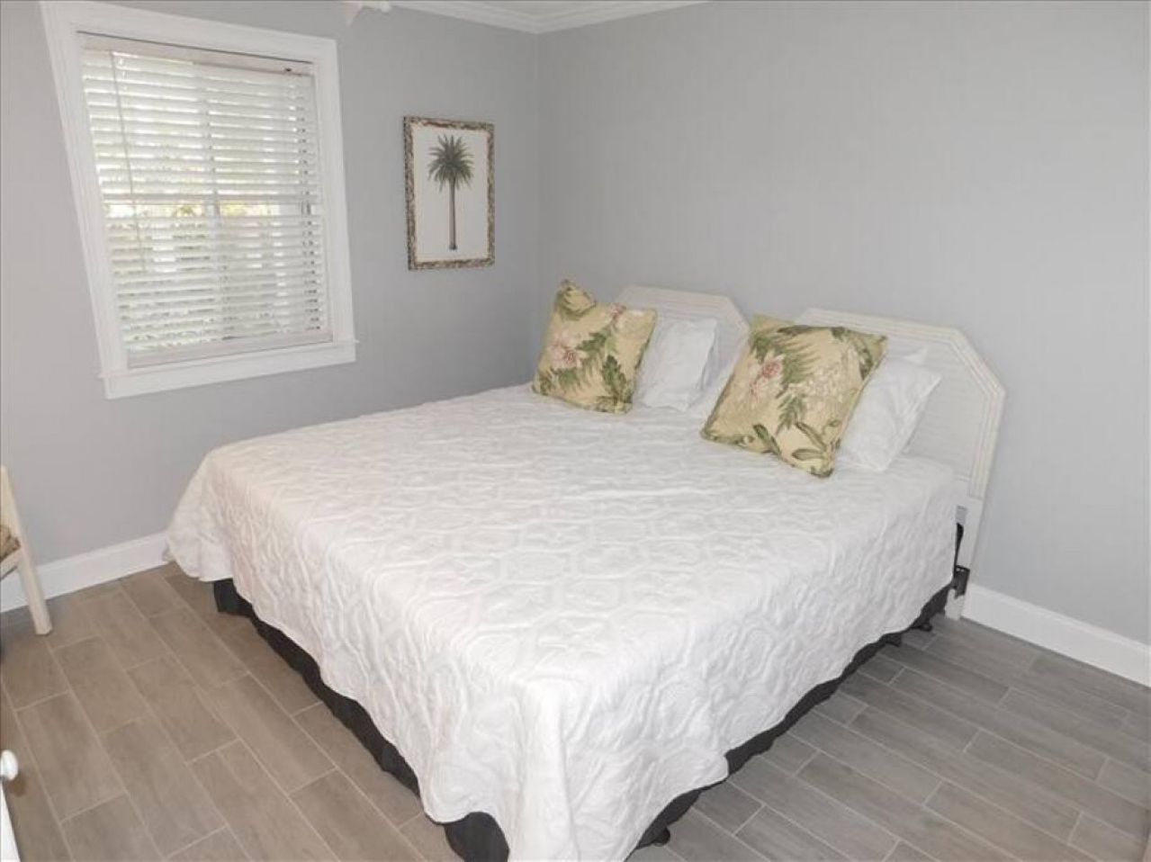 A bedroom with a bed, a window with blinds, and a framed picture on the wall.