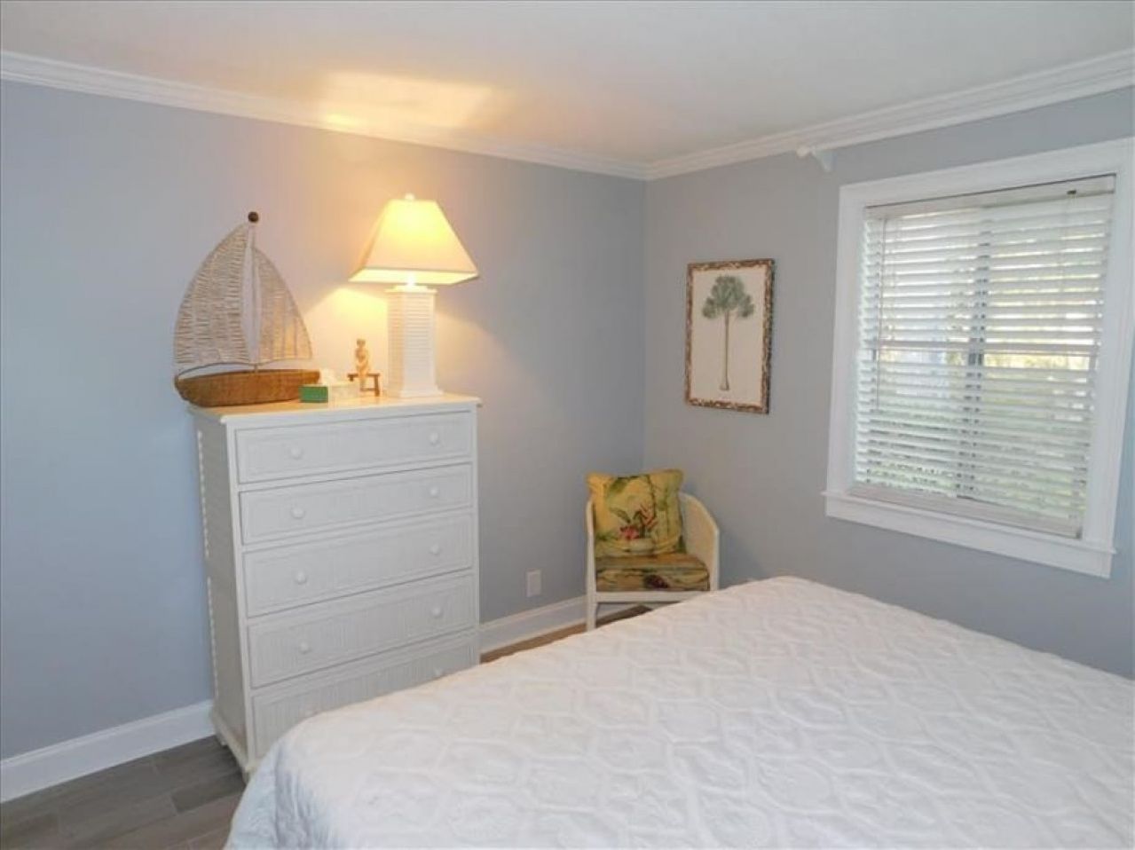 A bedroom with a bed, a dresser, a chair, a lamp, and a window with blinds.