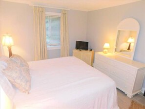 A bedroom with a bed, a dresser, a television, and a window with curtains. - E11 Peaceful 2/2 Ground Level, New Shower & Floors (St. Simons Island)