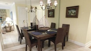 Un comedor con una mesa de madera oscura, sillas de mimbre y una araña.