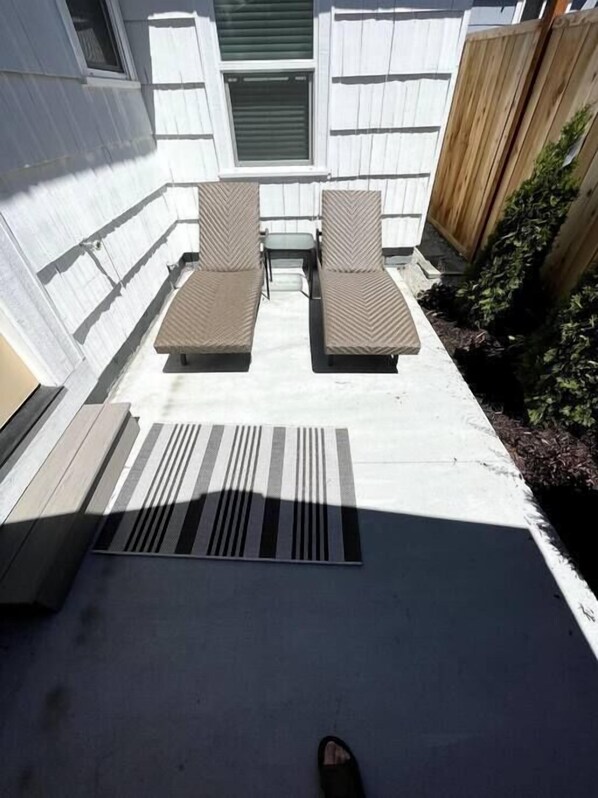 Une terrasse avec deux fauteuils rembourrés et une table, une bouche d’aération et une clôture en bois.