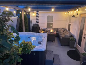 Une terrasse extérieure dotée d’un jacuzzi, d’un espace salon et de guirlandes lumineuses.