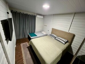 A small, compact room with a single bed, a television, and a window with curtains. - Casa Campeche - 100m da Praia (Florianópolis)