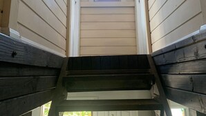 Eine Holztreppe führt zu einem kleinen Fenster mit Blick auf grüne Vegetation.