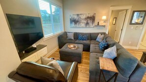 A modern living room with a flat-screen TV, grey sofas, a coffee table, and a wooden floor. - Edgewood Escape | Mt. Rainier View| EV Charger - Central (Edgewood)