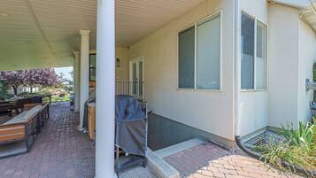 A covered patio with outdoor furniture, a grill, and a brick pathway leading to a house.