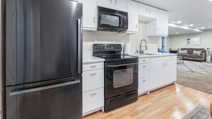 A modern kitchen with a stainless steel refrigerator, a microwave, an oven, and white cabinetry. - Private/clean guest suite, bath, kitchen & laundry (South Jordan)