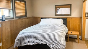 A bedroom with a bed, wooden paneling, a small bedside table, and a window with blinds. - Awesome Location Steam Shower Hottub (Telluride)
