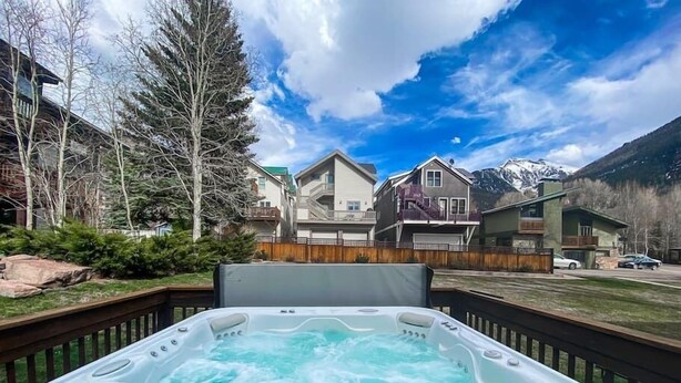 A hot tub with a wooden deck, surrounded by a wooden fence, with houses and mountains in the background. - Awesome Location Steam Shower Hottub (Telluride)
