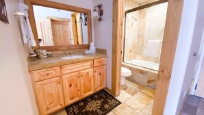 Un baño con armarios de madera, un espejo grande, un lavabo y una zona de ducha.