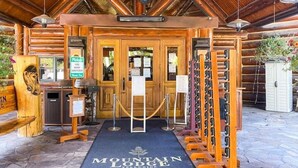 Entrada de una cabaña de madera con un letrero que dice Mountain Lodge, un dispensador de gel antibacterial y una estantería para vinos.