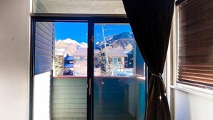Una porta a vetri scorrevoli conduce a un balcone con un pavimento in legno e vista su una montagna e una casa.