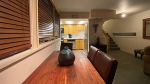 Zona pranzo con tavolo e sedie in legno, un vaso e una cucina sullo sfondo.