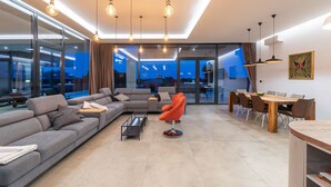 A modern living room with a grey sectional sofa, a red chair, and a dining area with a wooden table and chairs. - Luxury Villa Borealis with Pool (Ližnjan)