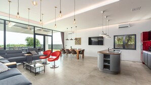 A modern living room with a grey sofa, red chairs, a glass coffee table, and a dining area with a wooden table and chairs. There is a kitchen with a grey island and red cabinets. - Luxury Villa Borealis with Pool (Ližnjan)