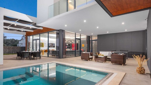 A modern outdoor pool area with a glass-enclosed dining space, outdoor seating, and a view of the adjacent building. - Luxury Villa Borealis with Pool (Ližnjan)