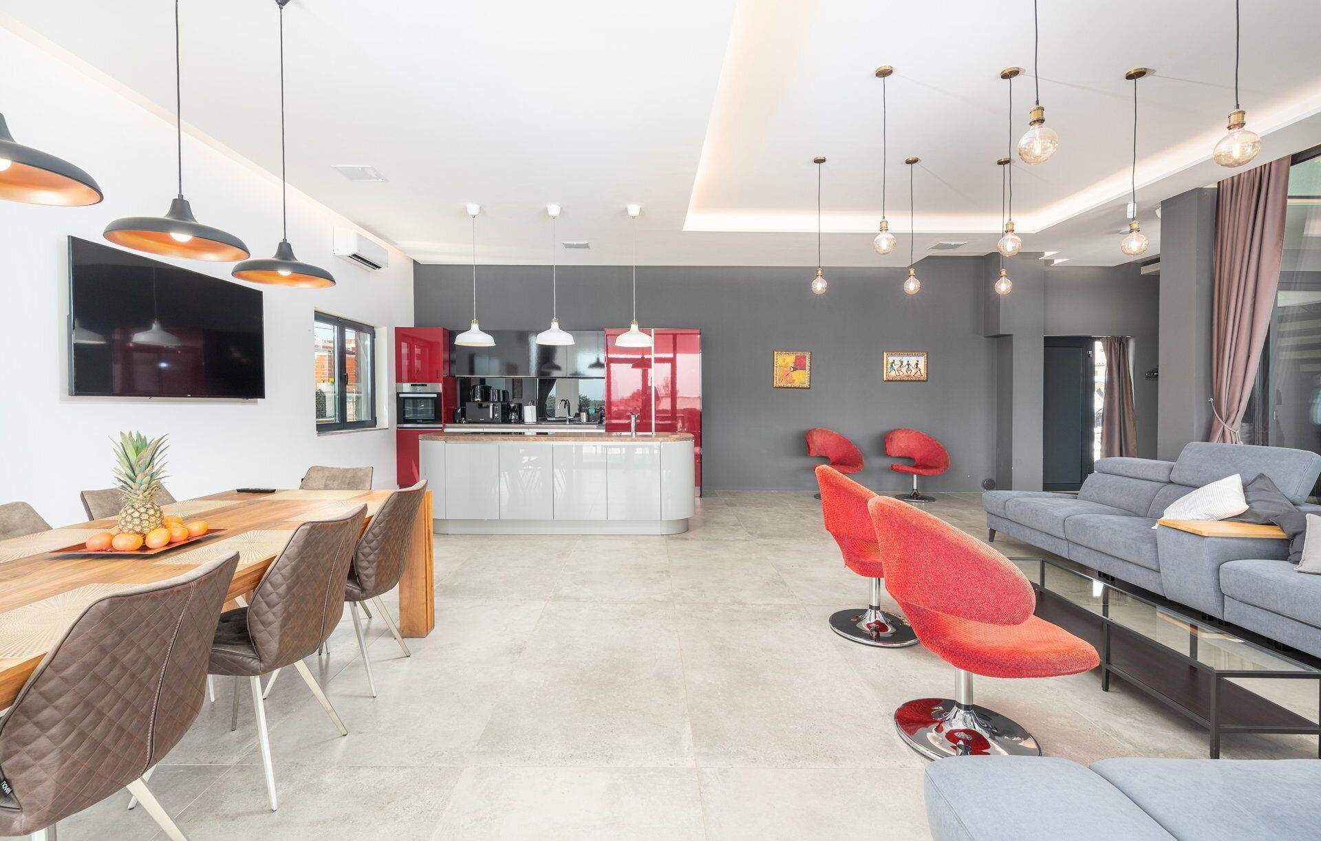 Une cuisine moderne dotée d’un îlot central, un coin repas avec une table et des chaises en bois, et un espace de détente avec un canapé et des fauteuils rouges.