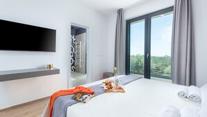 A modern hotel room with a large bed, a flat-screen TV mounted on the wall, a balcony with a view, and a small seating area with a table and chairs. - Luxury Villa Monroe with Pool (Vodnjan)