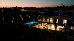 A modern two-story house with a swimming pool, a patio with outdoor furniture, and a view of the surrounding neighborhood at dusk. - Luxury Villa Monroe with Pool (Vodnjan)