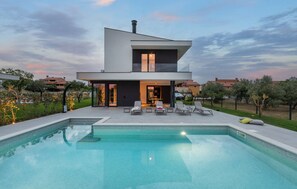 Ein modernes, zweistöckiges Haus mit Swimmingpool und Gartenmöbeln.