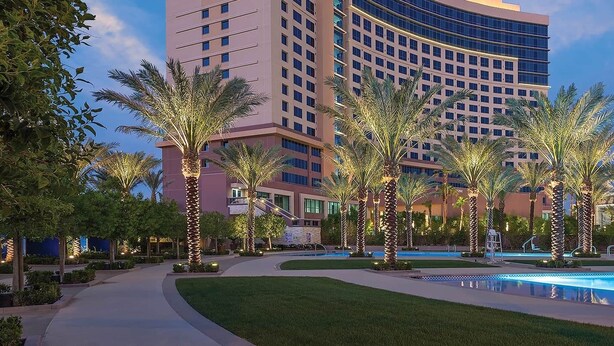 A hotel with a pool, palm trees, and a curved building facade. - 3BD/Vegas - Kitchen, Margarita Mixer, and Parking! (Las Vegas)