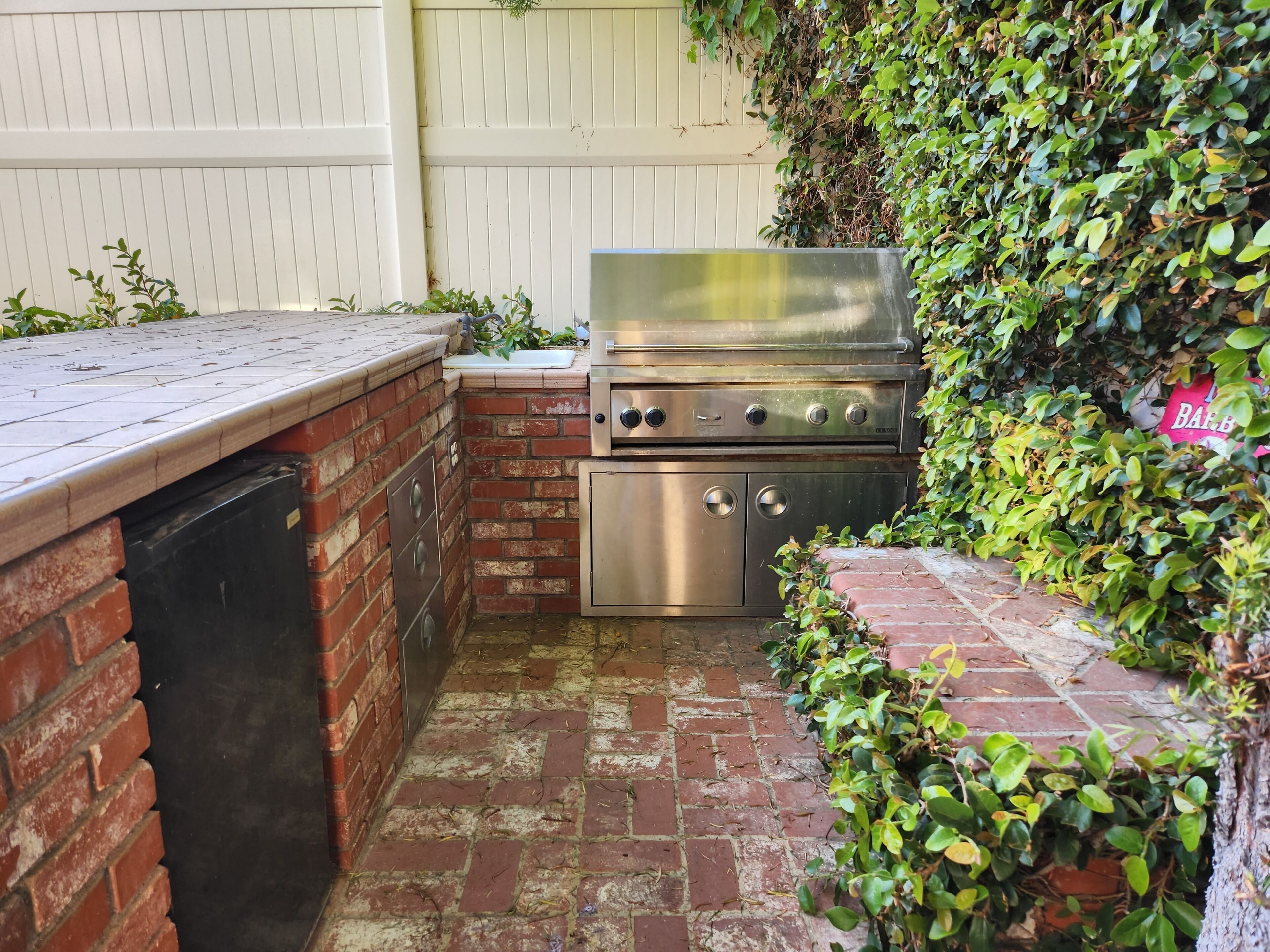 A brick outdoor kitchen with a stainless steel grill, a sink, and a countertop.