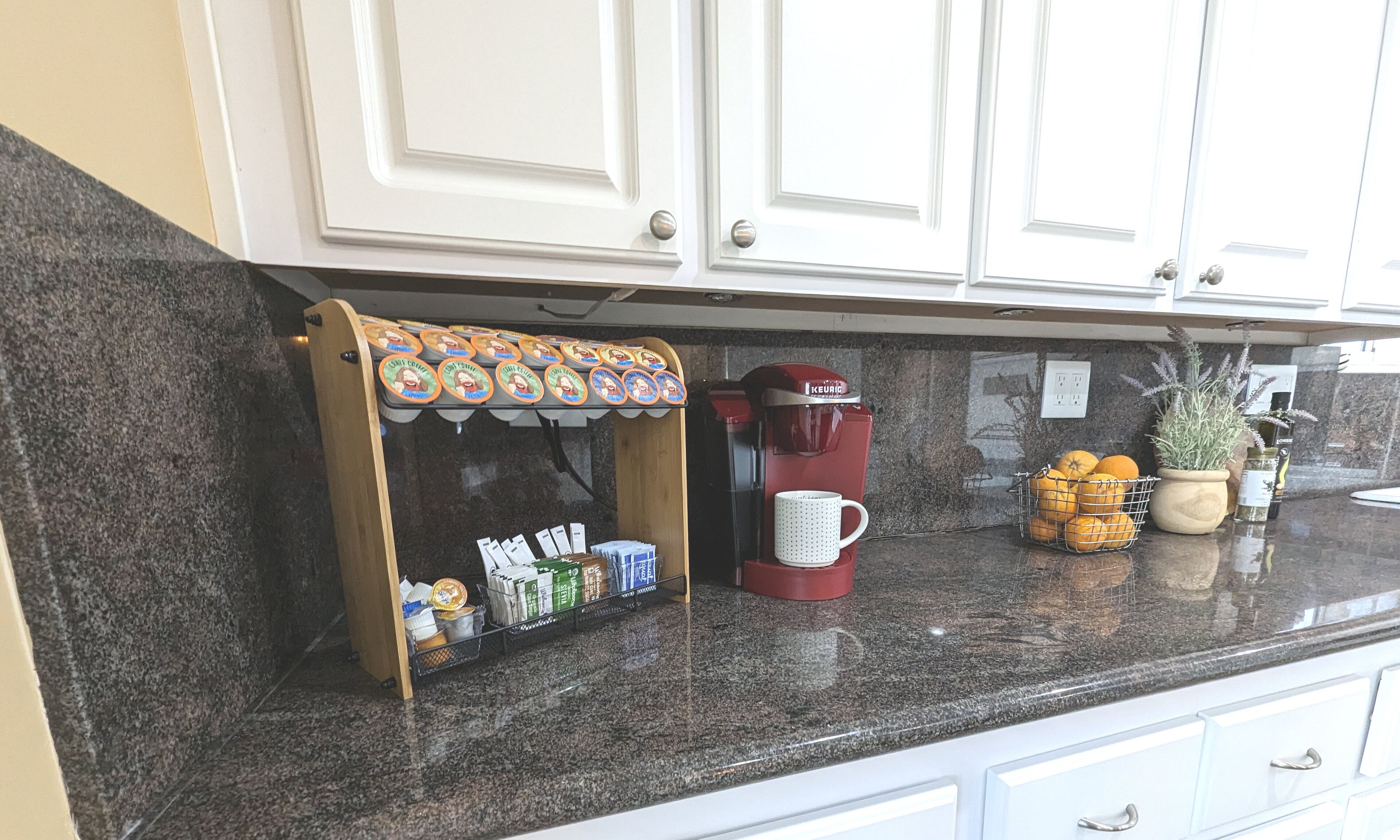 Eine Küche mit einer Kaffeestation, einer roten Keurig-Kaffeemaschine, einer Orangenschale und einer Blumentopf-Pflanze.