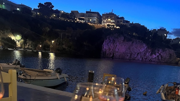 A table with plates of food and a glass of wine, overlooking a body of water with boats and buildings in the background. - Mary's Central Beachside Mansion- with large Terrace and Balcony  (Agios Nikolaos)