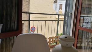 Un balcon donnant sur un immeuble avec un toit recouvert de tuiles et un panneau indiquant qu’il est interdit de se garer.
