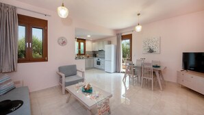 A modern living room with a sofa, a coffee table, and a TV. There is a kitchen area with cabinets and a refrigerator. - Villa Amelia in the Cretan nature, ideal for families  (Rethymno)