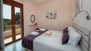 A bedroom with a bed, a window, a wall-mounted artwork, and a bathroom mirror. - Villa Amelia in the Cretan nature, ideal for families  (Rethymno)